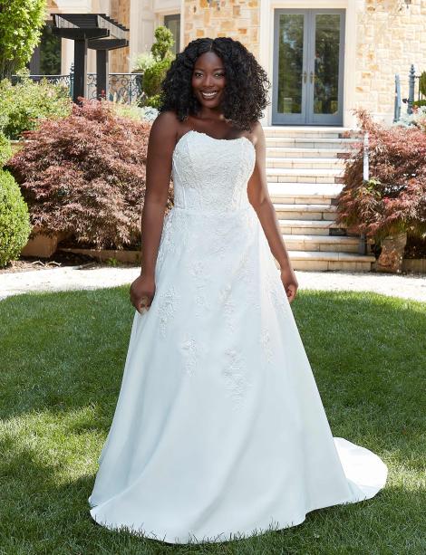Model wearing a wedding dress on a grass area in front of a house