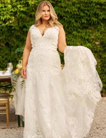 Plus size model wearing a beautiful wedding dress in front of green trees.