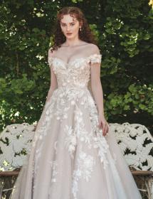 An innocent looking model standing in front of an ornate white lawn chair for two wearing an Allure Bridgerton wedding dress style number BR1008.