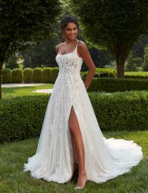 Model wearing a wedding dress on a grassy area in front of a hedge