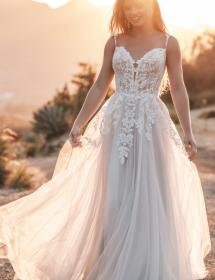 Model wearing a wedding dress in a desert like area with sun shining behind her head