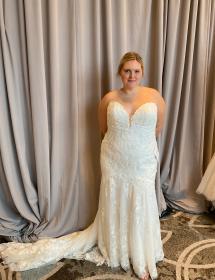 Plus size model wearing a stunning wedding dress in front of a grey curtain.