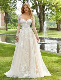 Plus size model wearing a stunning wedding dress on a grassy area in front of a pool with a fountain.