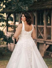 Plus size model wearing a stunning wedding dress in front of a jungle hut.