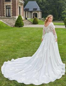 Plus size model wearing a stunning wedding dress in a garden with a house in the background.