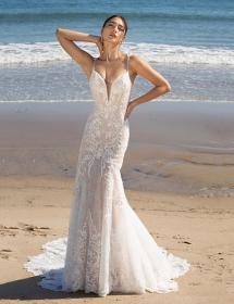 Model wearing a wedding dress on a beach looking like she is stretching.