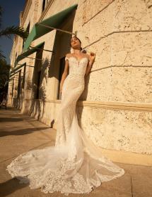 Model wearing a wedding dress sunning herself while leaning against an ornate building wall.