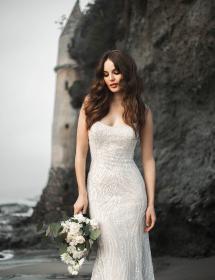 Happy model wearing a wedding gown in front of a beach cliff with a castle nearby