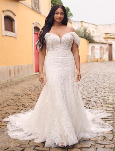 Plus size model wearing a beautiful wedding dress standing on uncomfortable cobblestones in front of a spanish looking house .