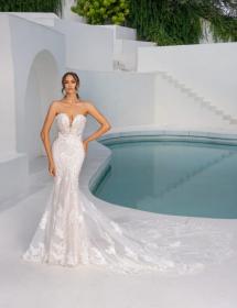 Women wearing a white wedding dress posing next to an elegant blue water pool.