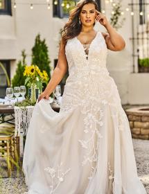Plus size model wearing a beautiful wedding dress in front of a nice table.