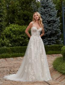 Model wearing a beautiful wedding dress in a garden on a path in front of mainicured bushes and trees..