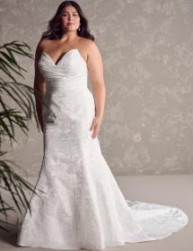 Model wearing a beautiful wedding dress in front of a textured wall with a plant on the right side.