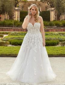 Plus size model wearing a stunning wedding dress in front of gardens.