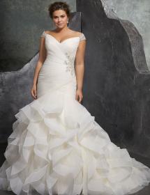 Plus size model wearing a stunning wedding dress in front of a curved wall.