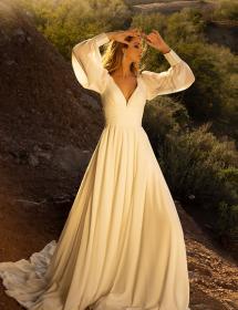 Model wearing a wedding dress on a hill with scrub brush in the background.