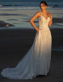 Plus size model wearing a stunning wedding dress on a beach with waves.