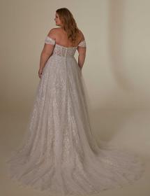 Plus size model modeling the back of an exquisite wedding dress in front of a creme colored curtain.