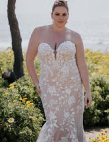 Plus size model wearing a beautiful wedding dress in front of a garden of wildflowers.