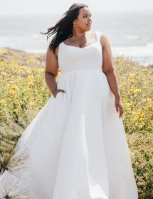 Plus size model wearing a beautiful wedding dress in a field of wildflowers with the coast in the background.