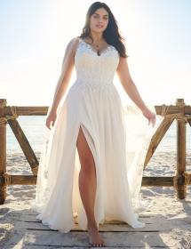 Plus size model wearing a beautiful wedding dress in front of a fence with sand and a beach behind.