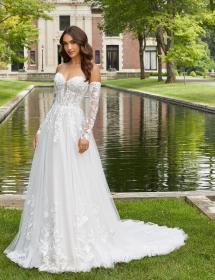 Model wearing a bridal gown in front of a pool with a house behind it.
