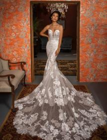 A woman models a wedding dress with a long trane in front of a chandelier and orange walls.