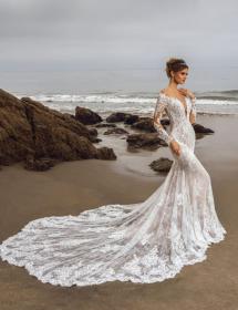 Happy model wearing a wedding gown on a beach with boulders in the near background 