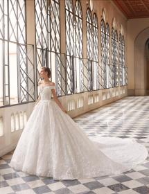 Happy model wearing a wedding gown in front of a curtain of windows in a grand hall.